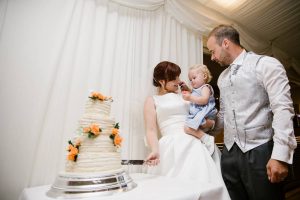 Bride cutting wedding cake with husband and baby